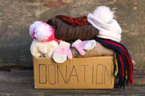 Donation box with warm winter clothes on old wooden background. Stock Photos
