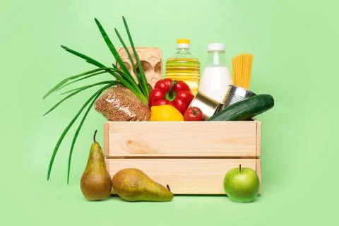 Donation or delivery wooden box with food on green background. Stock Photos