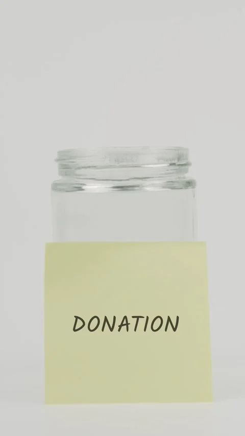 Donation text or word on yellow sticky note attached to glass jar with hand Stock Footage 311721417