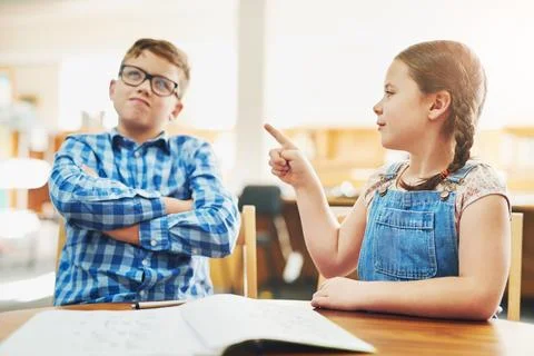 Dont be so grumpy. two young children working on schoolwork together while being Stock Photos
