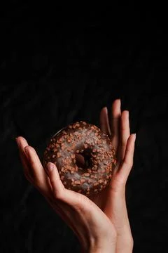 Donut in hands close up with dark background Photos