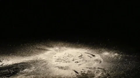 A donut with a sugar powder falls on a black desk Stock Footage