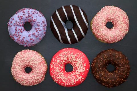 Donuts of different colors on dark background, view from above  Stock Photos