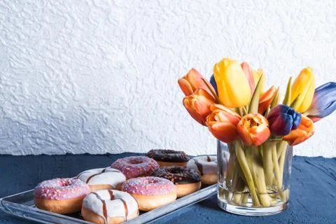 Donuts on a glass tray next to different colors tulips are in a vase Stock Photos