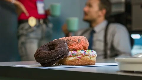 Donuts large in the foreground, in the background policemen drinking coffee. Video stock 70514093