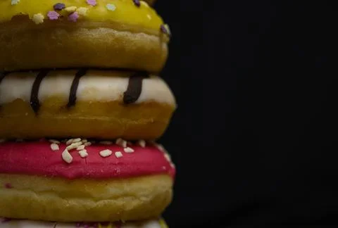 Donuts of multiple colors piled up close up Stock Photos
