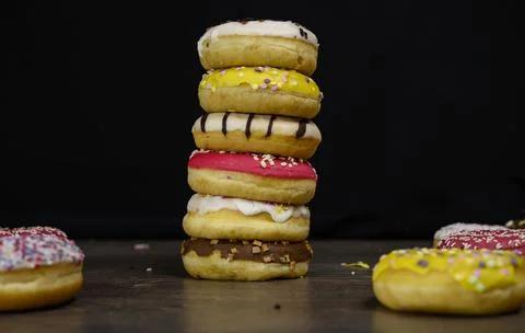 Donuts of multiple colors piled up close up Stock Photos