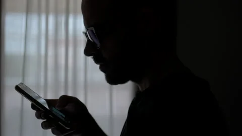 Doom scrolling. Silhouette of man scrolls page app on mobile phone. Cinematic Stock Footage 234147166