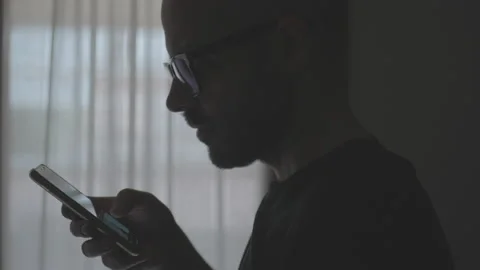 Doom scrolling. Silhouette of man scrolls page app on mobile phone. Cinematic  Stock Footage 234175438