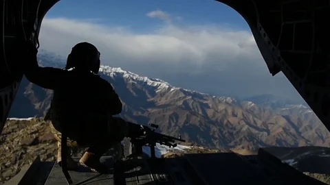 Door gunner crouching at rear open door of CH-47 Chinook above Afghanistan Stock Footage 87318834