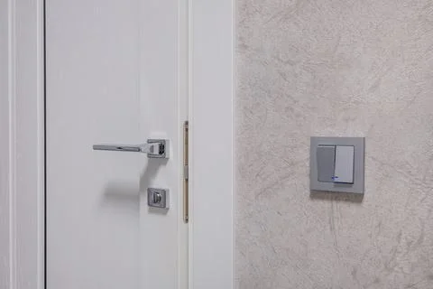 Door handle and light switch next to it in a bright room or office Stock Photos