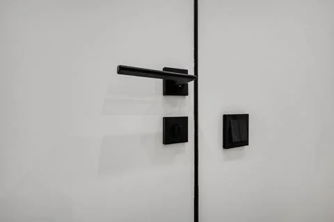 Door handle and light switch next to it in a bright room or office Stock Photos