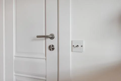 Door handle and light switch next to it in a bright room or office Stock Photos