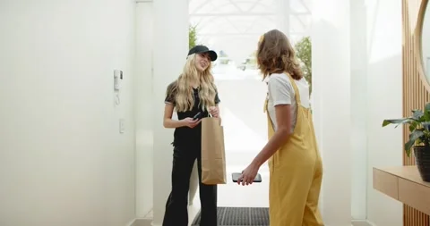 Door opening delivery worker stepping inside holding bag and device, homeowner Stock Footage 340454367