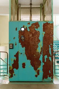 The door of a very old elevator with peeling blue paint and traces of rust Stock Photos