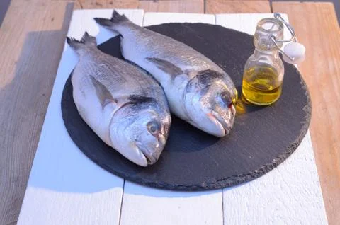 Dorado fish on a black plate with olive oil bottle Stock Photos