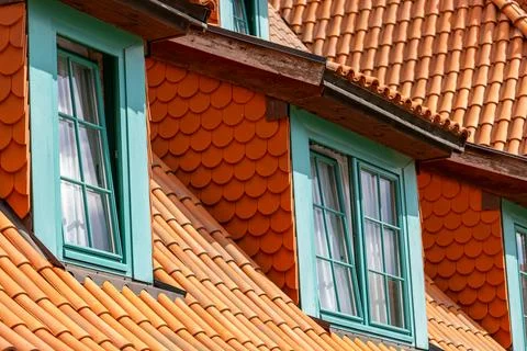 Dormer windows with turquoise wooden frames sit among orange terracotta roof. Фото