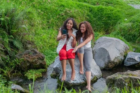 Dos vlogger de ecuador senrientes y sentadas en una gran roca dentro de un rio Stock Photos