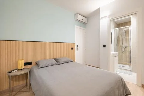Double bed with gray linen, small bedside table and wooden slats on the wall Stock Photos