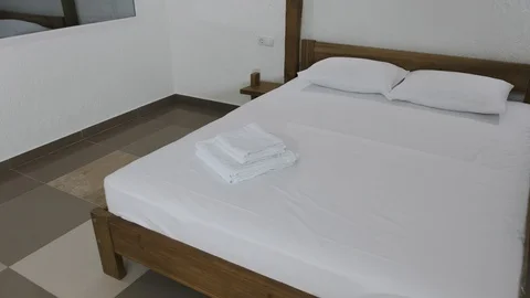 A double bed is standing on a tiled floor in a hotel room with mirror on a wall Stock Footage 89914961