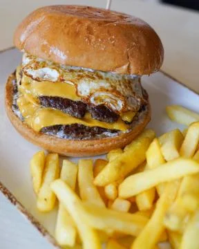 Double Cheeseburger with Fried Egg and French Fries on a Plate Fotos Stock