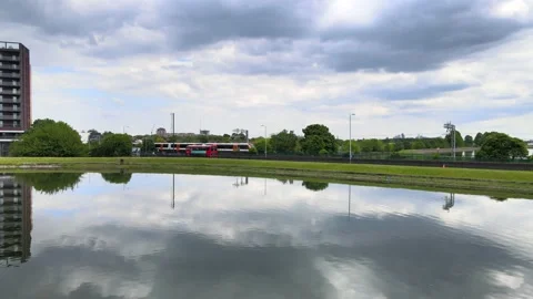 Double-decker and train running parallel around calm water surface Stock-Footage 155789265