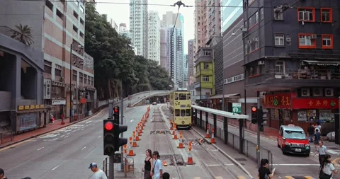 Double-decker tram and red taxi moving through busy Hong Kong street Видео 330953861