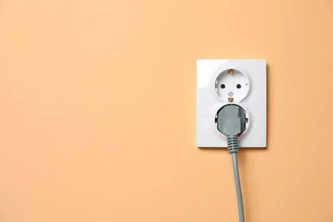 Double power socket with inserted plug on pale orange wall, space for text. E Stock Photos