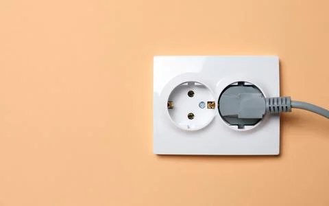 Double power socket with inserted plug on pale orange wall, space for text... Stock Photos