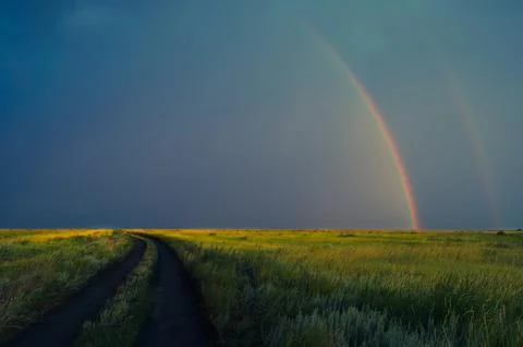 Double rainbow after rain on the background of storm clouds.Road in field. Stock Photos