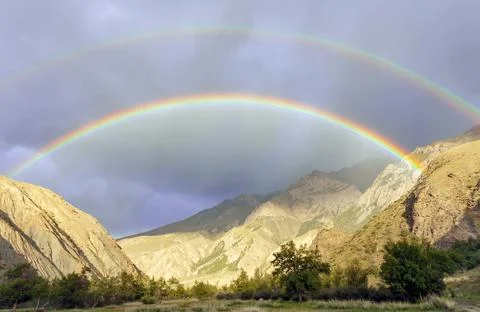 Double rainbow and heavy rain over the mountain valley. Stock Photos