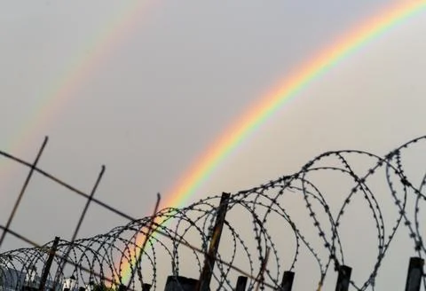 Double rainbow behind rows of a barbed wire. LGBTQ freedom suppression concept. Stock Photos