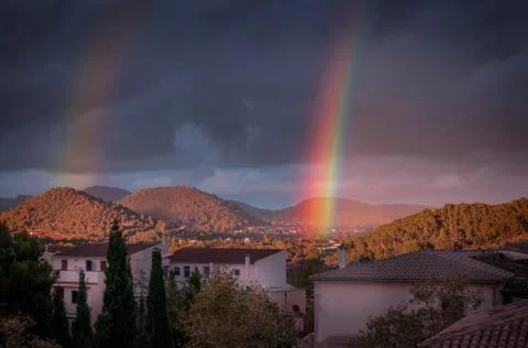 Double rainbow with dark, moody dramatic sky, forests and hills in the backgr Stock Photos