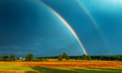 Double rainbow over the field, on which cows are grazed, in darkly blue sky a Stock Photos