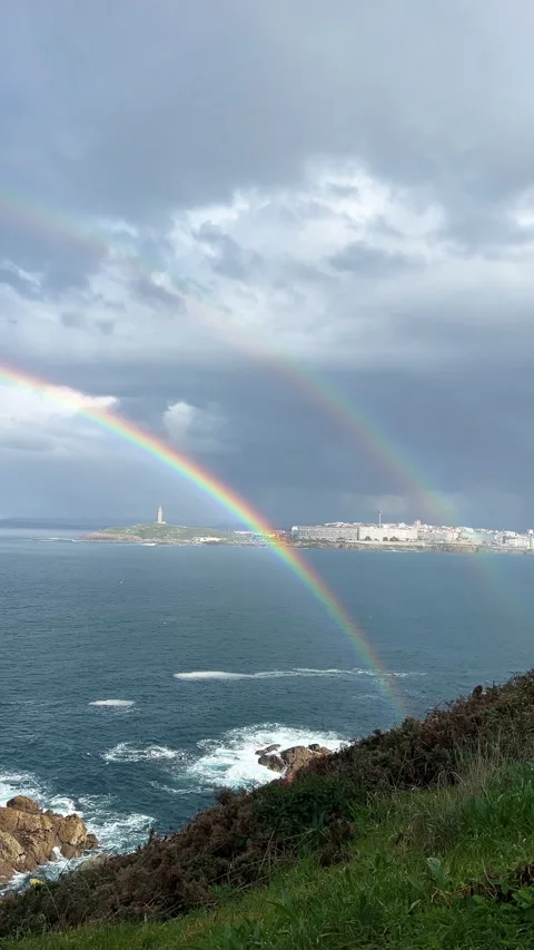 Double rainbow over rocky coast and city skyline by the sea Stock Footage 313193650