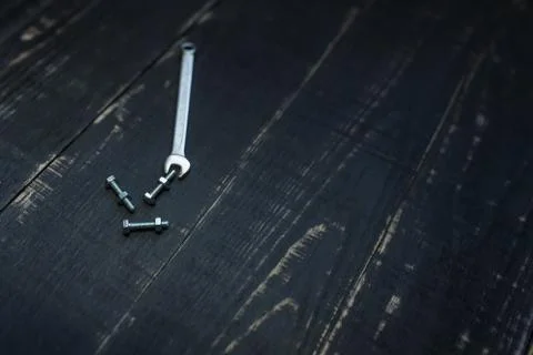 Double sided key, some nuts and bolts on black wooden background. Stock Photos