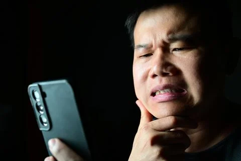 Doubtful man reacting to smartphone content with uncertain facial expression 스톡 사진