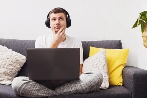 Doubtful young man looking up while working on laptop Stock Photos