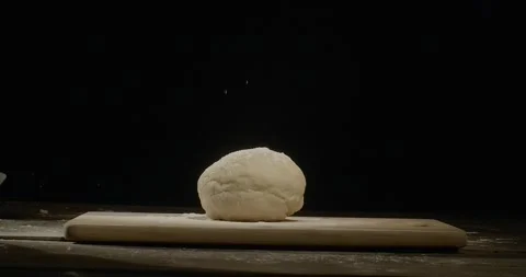A dough on a black background. Hands sprinkled flour on the dough and kneading 動画素材 229708452