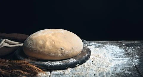 Dough on a board among flour and wheat on a black background. Stock Photos