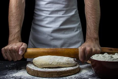 Dough on a dark background. The cook works with the dough on a black background. Stock Photos