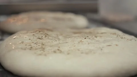 Dough rising on a baking tray with visible texture and seasoning, showcasing the Vídeo Stock 331755476