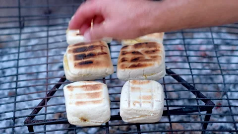 Dough rolls (roosterkoek) on grid being grilled over hot coals turned by hand Stock Footage 332610766