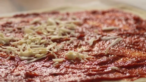The dough is spread with tomato sauce and sprinkled with shredded cheese. Stock Footage 266900312