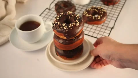 Doughnut on the baking rack glazed with chocolate cream or icing. Woman hand put Stock Footage 145121660