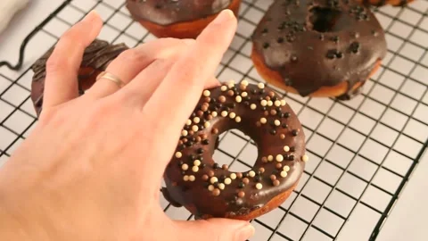 Doughnut on the baking rack glazed with chocolate cream or icing. Woman hand put Stock Footage 145121715