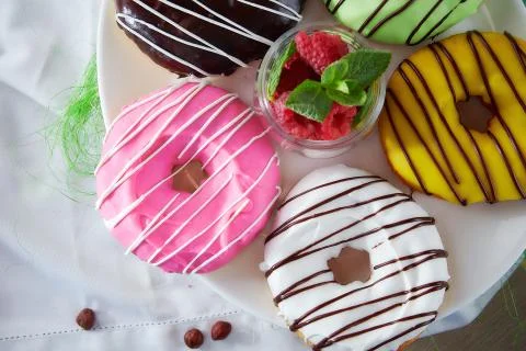 Doughnuts with multi-colored glud on white tablecloths and raspberries Stock Photos