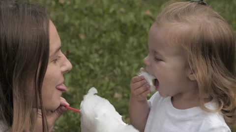 Doughter with mom in the park having fun and sharing cotton candy. 库存影片 99487388
