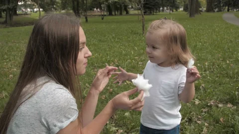 Doughter with mom in the park having fun and sharing cotton candy. 库存影片 99488097