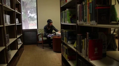 Down the aisle looking at teen in library, medical mask pulled down Stock Footage 134671301
